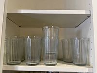 Shelf containing eight tall clear ribbed glass tumblers