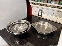 Three nesting stainless mixing bowls beside one shallow handled bowl