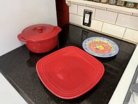 All three items on countertop: red casserole with lid, red square platter, Sango fruit plate