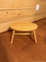 Round wooden footstool on floor, showing seat, legs, stretcher