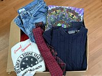 Box containing jeans, Grateful Dead tee, Oscar de la Renta sweater, two red ties, white event tee
