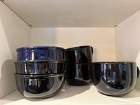 Stack of four black bowls and three black mugs inside a shelf