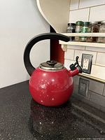 Front view of red Circulon whistling teakettle on countertop