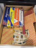Drawer with four boxed rolls (foil, plastic, waxed, parchment) and assorted reusable cloth food wraps