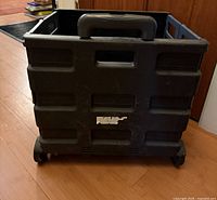 Front view of folded rolling crate showing side panels, handle grip and front wheels