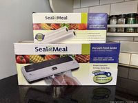 Boxed SealaMeal vacuum food sealer and separate box of two sealing rolls