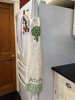 Apron hanging on refrigerator showing full length, checkerboard hem, word “Artichoke” visible