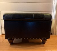 Front view black leather ottoman showing nailhead trim and turned legs