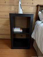 Full view of rectangular black open-shelf nightstand beside bed