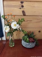 Two artificial arrangements on tabletop: glass vase with faux flowers, ceramic bowl with succulents