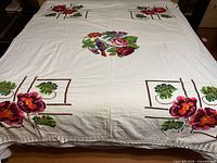 Full view of embroidered top sheet on bed showing central bird and roses motif and corner floral panels