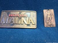 Honda Magna brass belt buckle beside Cavalier medallion