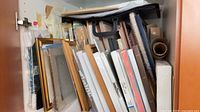 Cabinet shelf filled with assorted frames, canvases, roll