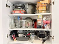 Cabinet shelves showing bulk of bakeware, pans, bowls, utensils