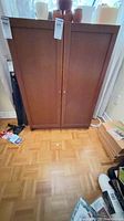 Full view of brown laminate two-door cabinet standing on parquet floor