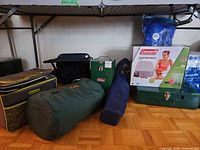 Group view of camping items including stove, sleeping bag, chairs, air mattress box
