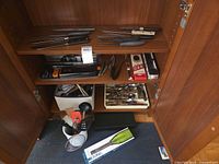 Cabinet showing assorted knives, packaged Staysharp knife, utensil bin, flatware tray, wine chiller box