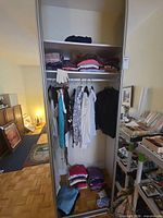 Full wardrobe view showing folded garments on shelf, hanging blouses and tops, folded sweaters at bottom
