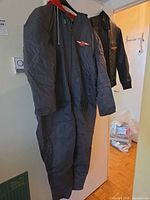 Gray snowsuit hanging with leather coat behind, showing overall form and patches