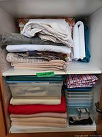 Cabinet showing two shelves with stacked fabrics and multiple clear plastic containers