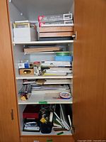 Full cabinet view showing frames, papers, paints and tools on multiple shelves