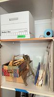 Shelves showing Bankers Box, patterned box with frames, brass easels, blue roll, mats