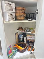 Cabinet view with boxed casserole dishes, clay bowls, rack, utensils and packaged items