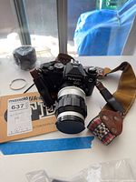 Front view of Nikon FE camera with attached 135 mm lens, strap, and manual visible