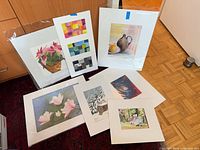 Group shot of seven of the eight matted paintings laying against cabinet and floor