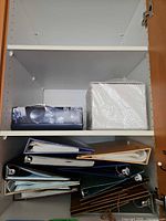 Cabinet shelf with eight assorted hard-cover photo albums and bubble-wrapped box