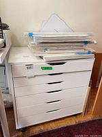 Front view of white six-drawer cabinet on casters with stack of art on top