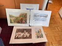 Group view of matted paintings standing and lying on rug