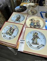 Eight Goebel Hummel porcelain decorative plates—four boxed, four loose—displayed on a table