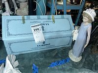 Lladró figurine standing beside original blue Lladró box displaying lot tag