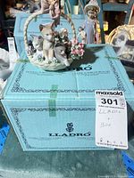 Figurine atop original blue Lladró box with auction tag visible