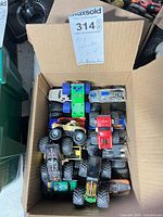 Cardboard box containing roughly 15 assorted monster truck toys