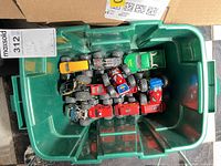 Top view of green bin containing approximately 15 monster trucks