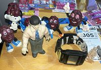 Overview showing four California Raisins figures, one human figure, and digital watch on tabletop
