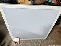 Front view of square white LED panel leaning against wall with small accessory box for scale