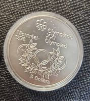 Obverse of coin in capsule: Olympic rings laurel design, text Montréal 1976, denomination