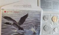 Envelope with loon illustration and visible plastic holder containing four of the coins