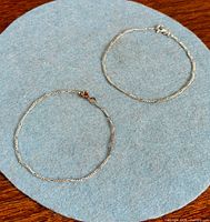 Two figaro link sterling bracelets laid flat on felt