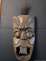 Front view of carved wooden mask showing facial details, open mouth and horsehair tuft