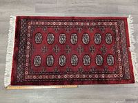 Full view of red hand-knotted rug with fringe and ruler for scale