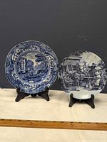Front view of both Delft blue plates on black stands with ruler for scale
