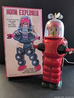 Front view of red tin Moon Explorer robot beside original box