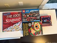 All four boxed items laid out: Scrabble Tile Lock, Chinese Checkers & Tiddly Winks, Lego City 60084, Cars puzzle