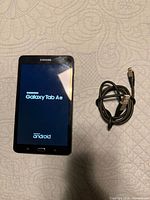 Front view of Samsung Galaxy Tab A tablet powering on beside included USB charging cable