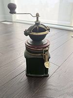 Front view of complete antique coffee grinder showing ceramic base, metal mechanism, brass crank, wooden knob