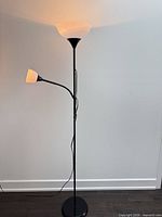 Full view of black torchiere floor lamp with main uplight and side reading light illuminated